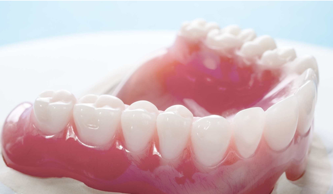 Dental prosthetic model showing upper teeth arrangement and pink gum tissue on white surface.