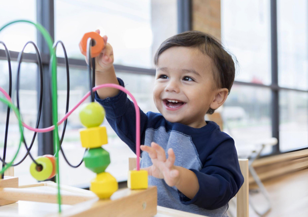 Smiling toddler playing with colorful toys in a bright, modern dental office setting.