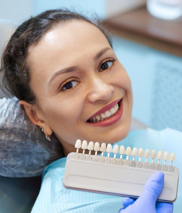 Woman smiling at dental office holding tooth shade guide for cosmetic dentistry consultation.