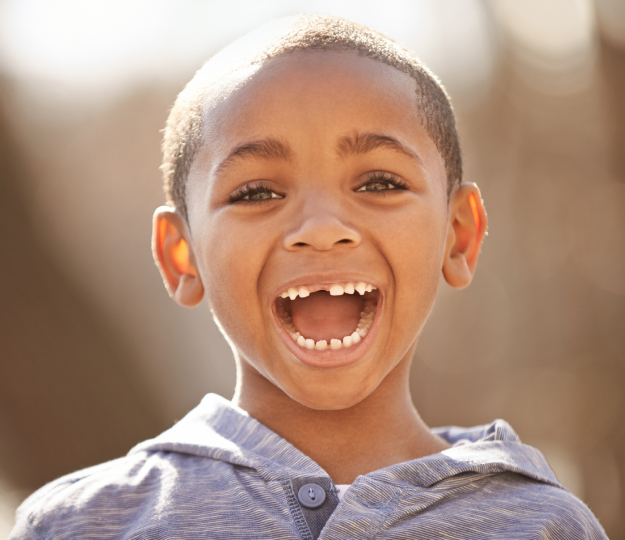 Young boy smiling brightly at camera in natural outdoor sunlight.