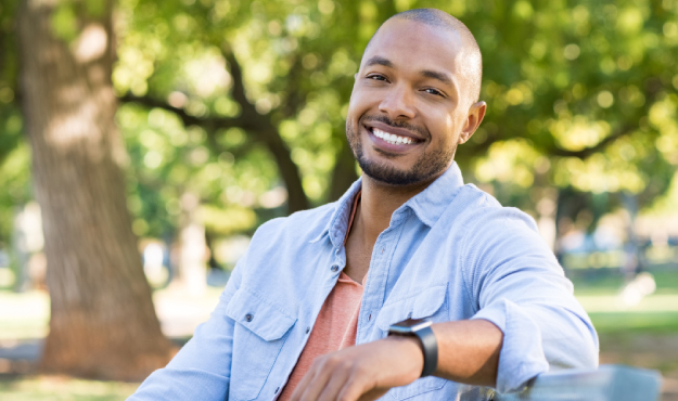 Smiling man in blue shirt posing outdoors in park setting for dental practice website.
