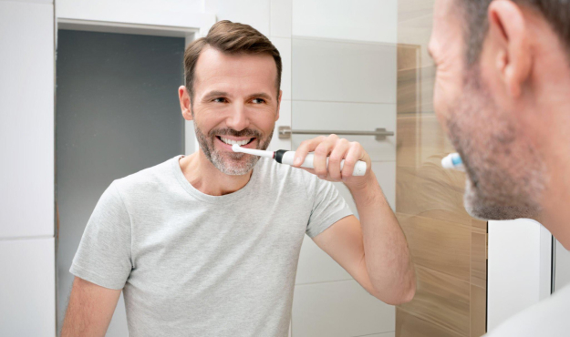 Man brushing teeth in bathroom mirror wearing casual shirt