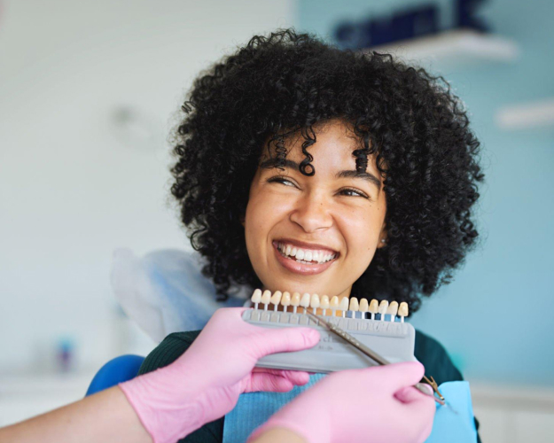 Smiling woman in pink gloves holding toothbrush in dental office setting.