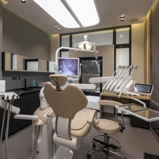 Modern dental operatory with cream-colored chair, overhead lighting, and dental equipment in professional clinic setting.
