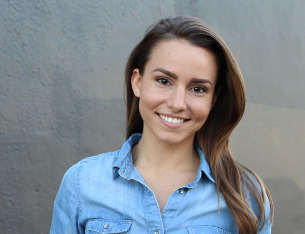 Smiling woman in light blue shirt against gray background, professional headshot for dental practice.