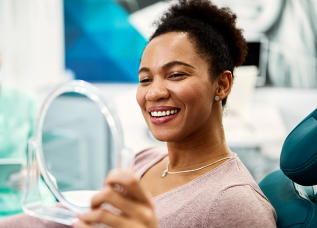 Woman smiling while holding mirror in dental office setting.