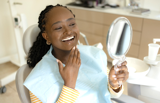 Woman smiling at mirror in bathroom, touching her face, demonstrating dental care and oral hygiene confidence.