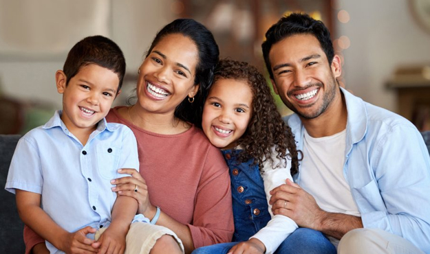 Happy family of four smiling together indoors at home, promoting dental care and family wellness.