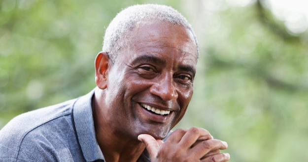 Smiling man resting chin on hand outdoors with blurred green background