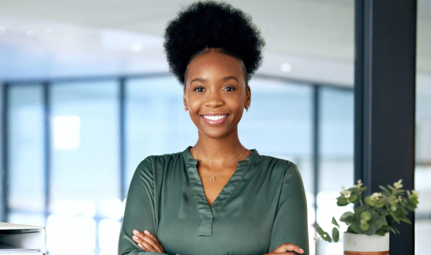 Smiling woman with arms crossed in modern dental office with windows and plants.