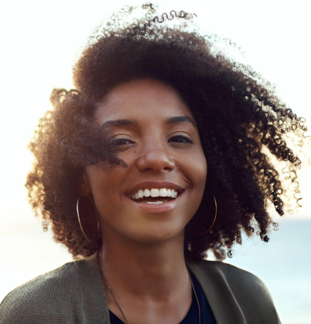 Smiling woman with curly hair wearing hoop earrings outdoors in natural sunlight