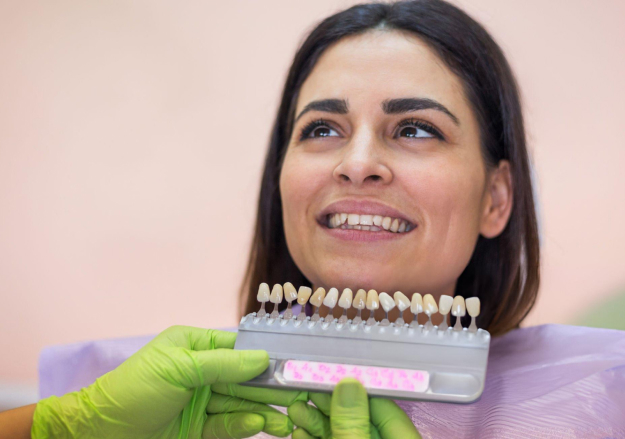 Dental professional in green gloves holding tooth shade guide for color matching in dental office.