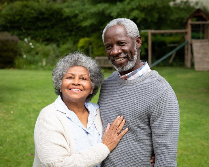 Smiling older couple posing together outdoors in garden setting for dental practice.