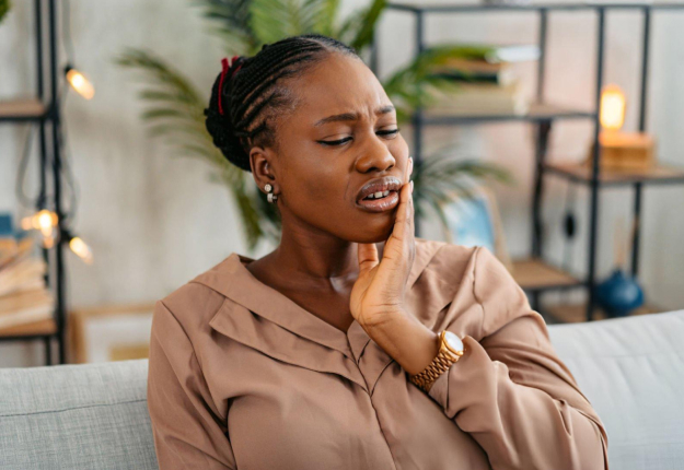 Woman touching her cheek in discomfort, sitting on couch in modern home setting.