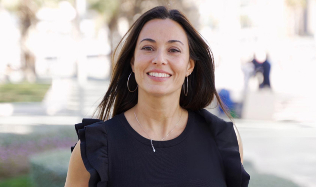 Smiling woman in black top outdoors at dental practice, professional headshot portrait.