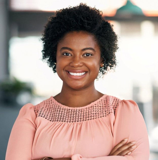 Smiling woman in pink top with arms crossed, professional dental office background