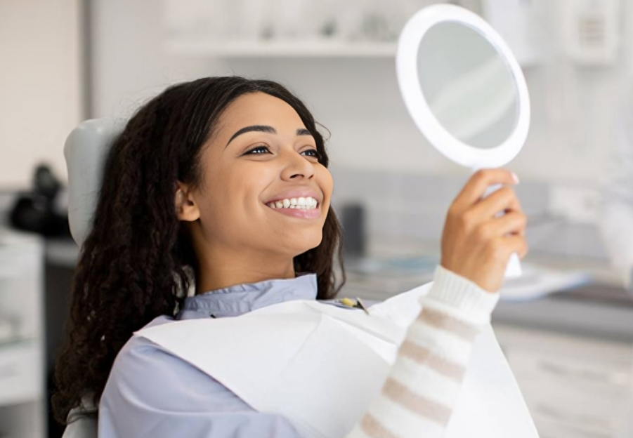 Smiling woman holding dental mirror in modern dentistry office examining teeth.