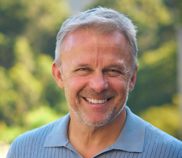 Smiling male dentist in blue shirt outdoors with blurred green background