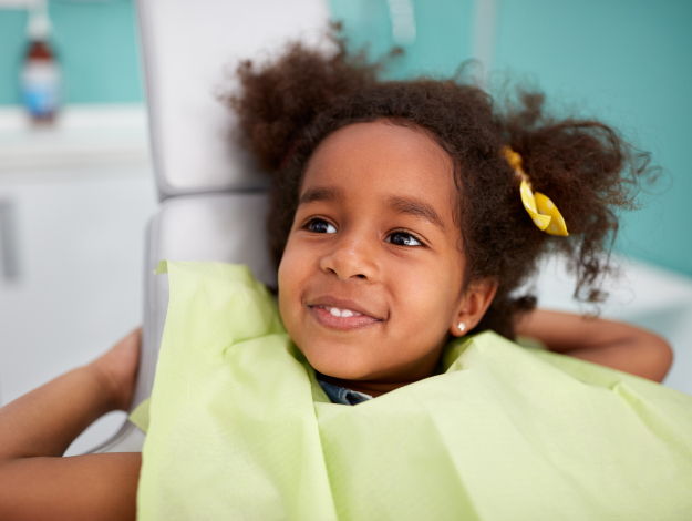 Happy child in yellow shirt smiling at dental office with turquoise background.