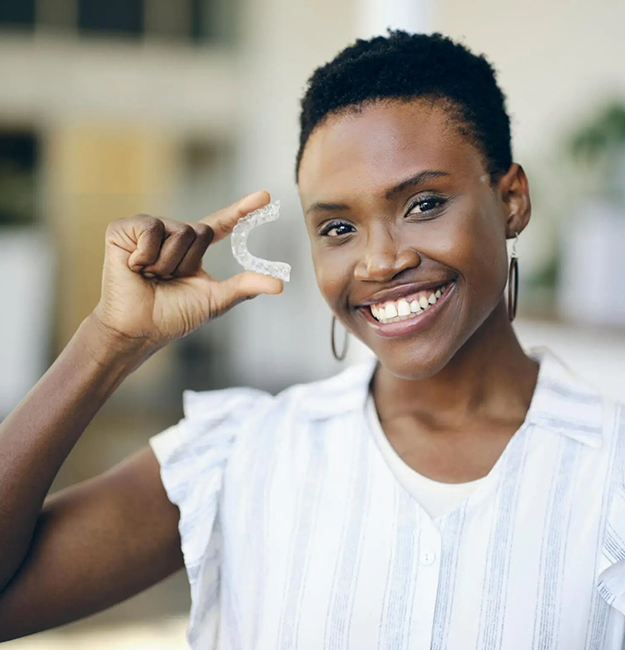 Smiling woman making small gesture with fingers in dental office setting, promoting family dentistry services.