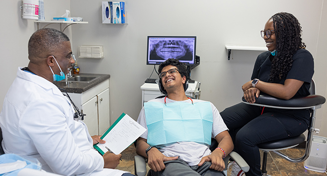 Dentist examines patient in dental chair while assistant observes in modern clinic setting.