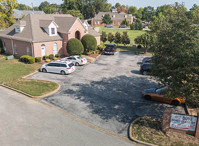 Residential neighborhood street with brick homes, parked cars, and manicured lawns on sunny day.