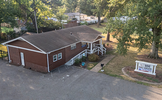 Red brick dental office building with entrance ramp surrounded by trees and landscaping.