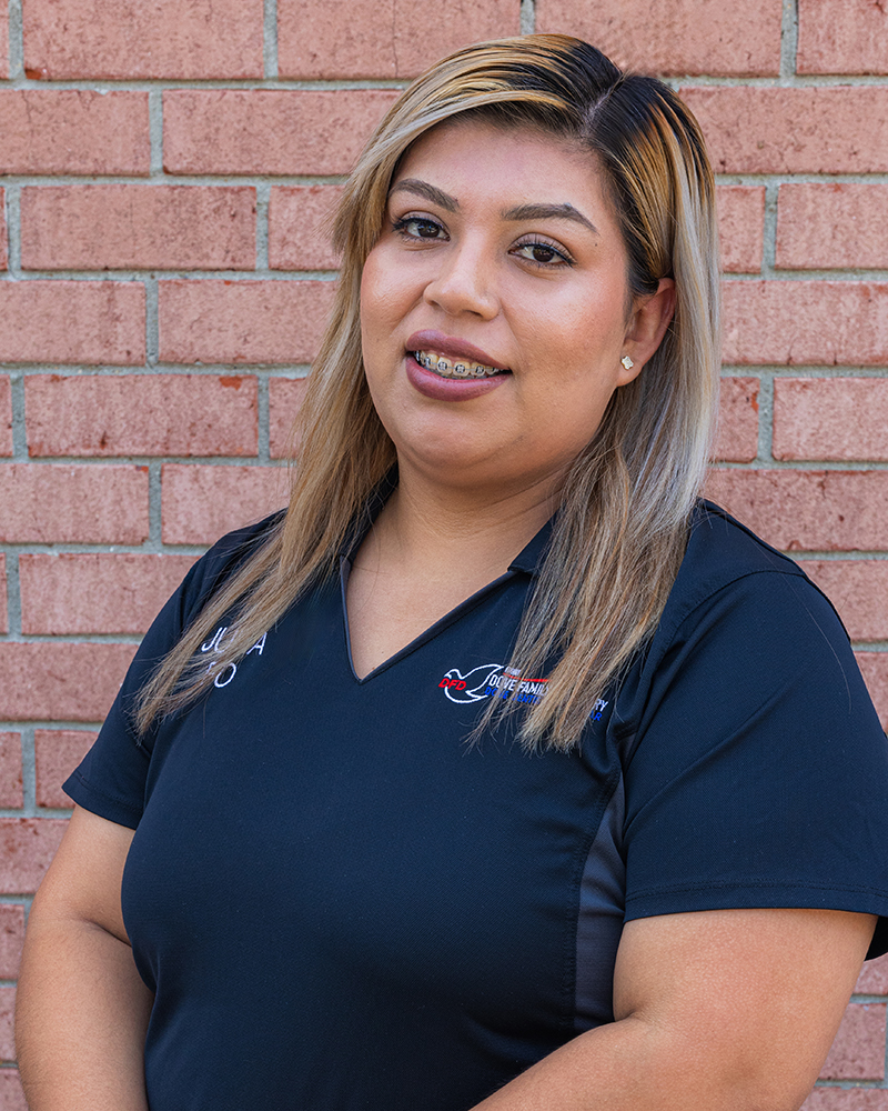 Professional woman in navy scrubs smiling against brick wall at dental office.