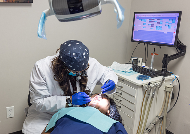 Dentist in blue gloves examines patient wearing protective eyewear in modern dental operatory.