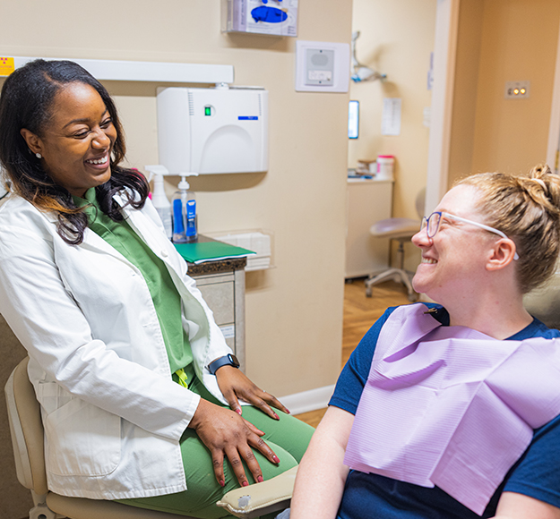 Female dentist in white coat examines patient's arm in dental office treatment room.