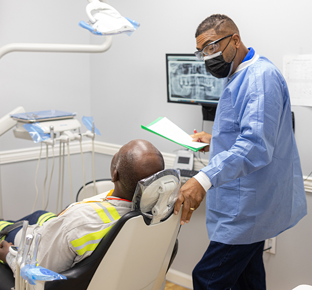 Dentist in blue scrubs examining patient's teeth in modern dental office treatment room.