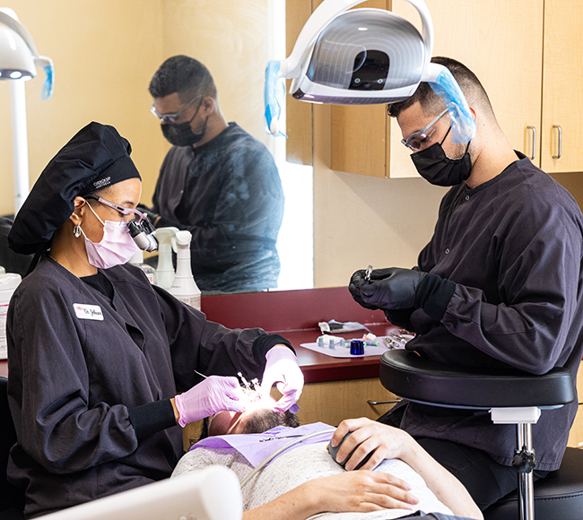 Dental hygienist examining patient's teeth under overhead light in clinical treatment room.