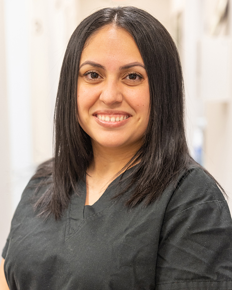 Professional headshot of smiling woman in dark scrubs at dental office.