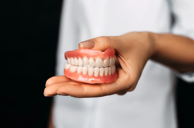 Person holding dentures model demonstrating dental prosthetics in clinical setting.