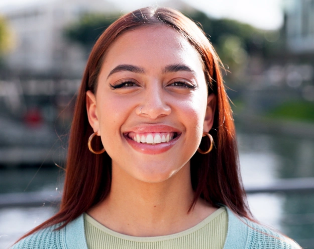 Smiling woman with reddish-brown hair wearing hoop earrings near waterfront setting