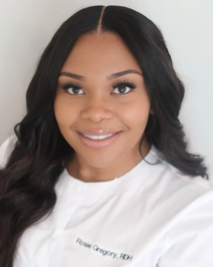 Professional headshot of smiling woman in white dental coat against neutral background.