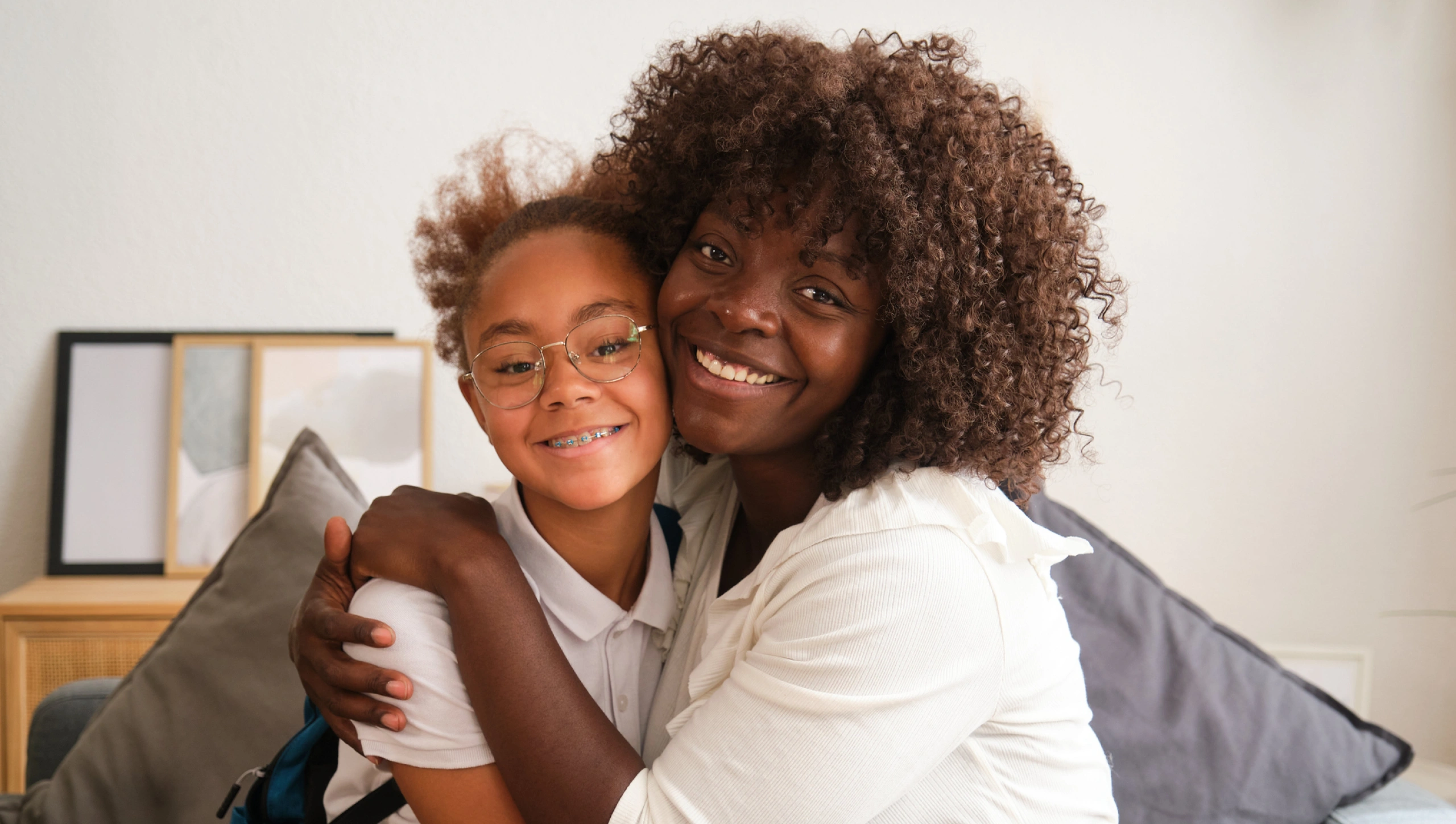 Mother and child smiling together indoors, embracing on couch with pillows.